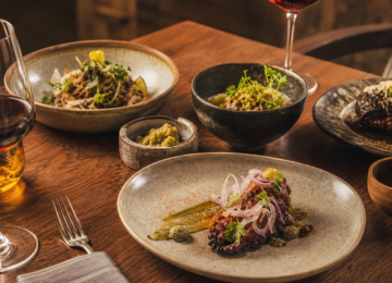 Mesa de cocina mexicana contemporánea con platillos, ingredientes locales y copas de vino.